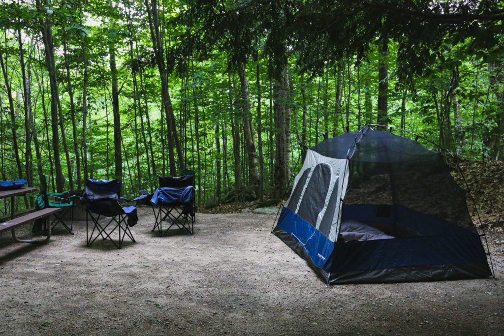 blue and white dome tent and camping chairs surrounded by trees