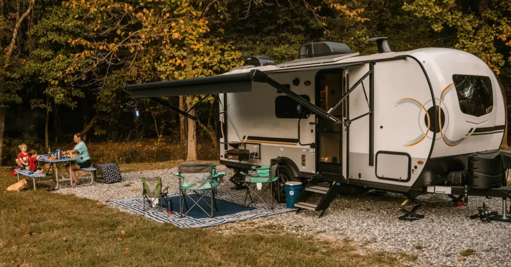 Family eating at a picnic table beside a travel trailer at a wooded RV campground