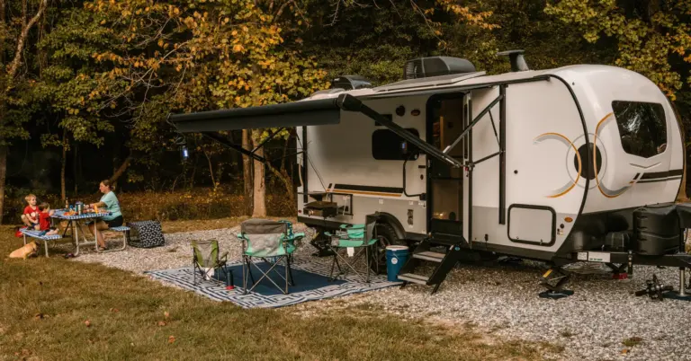 Family eating at a picnic table beside a travel trailer at a wooded RV campground
